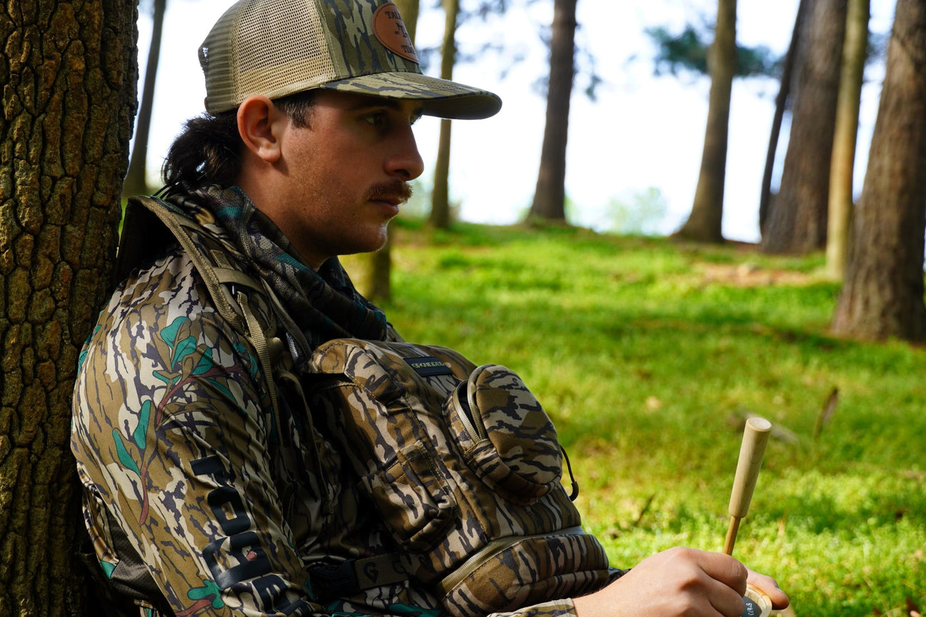 Calling turkey from the woods, laying up against a tree wearing a Talkin' Timber hat.