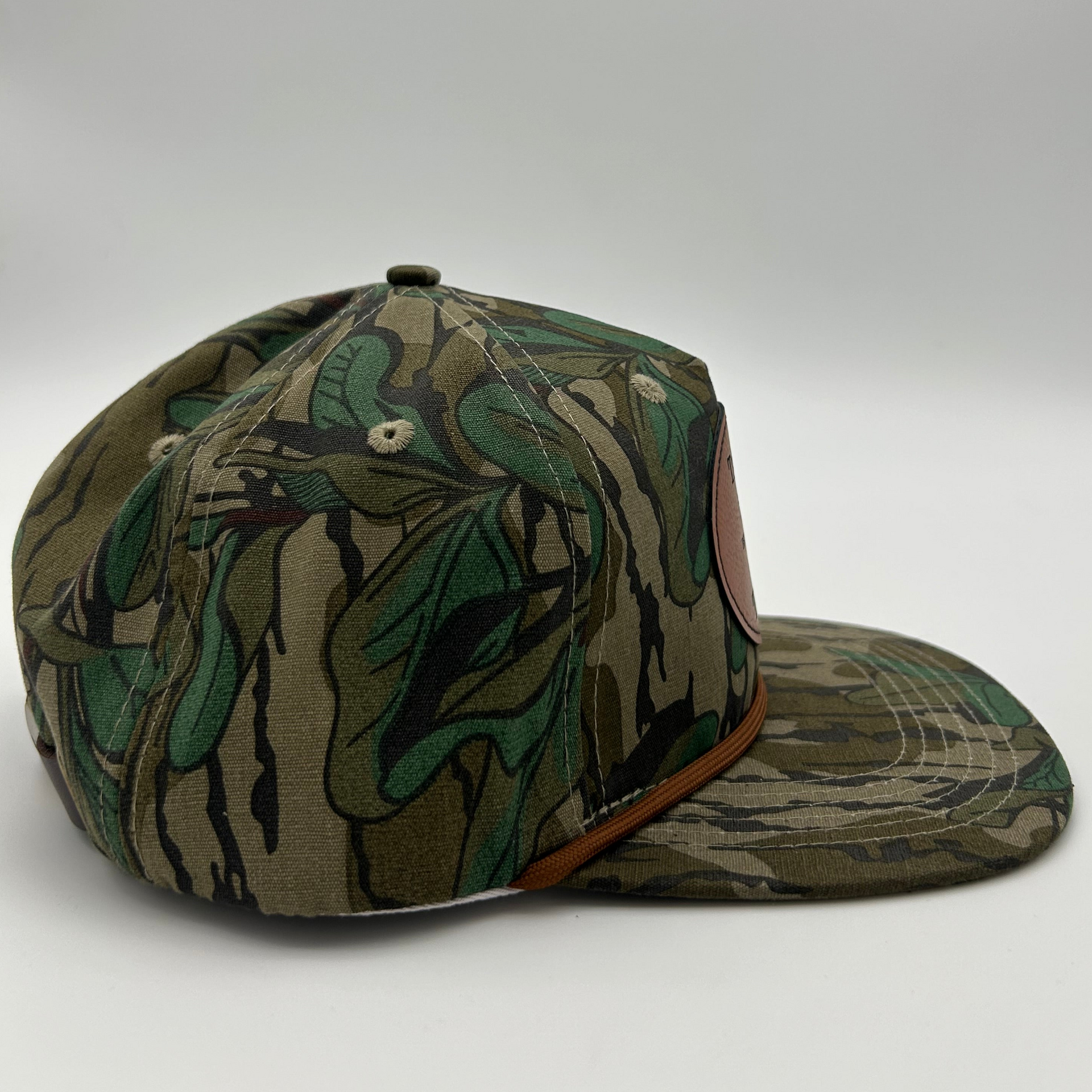 Side view of Mossy Oak™ Greenleaf rope hat featuring classic camo pattern and genuine leather patch, perfect for duck, turkey, or deer hunters. 